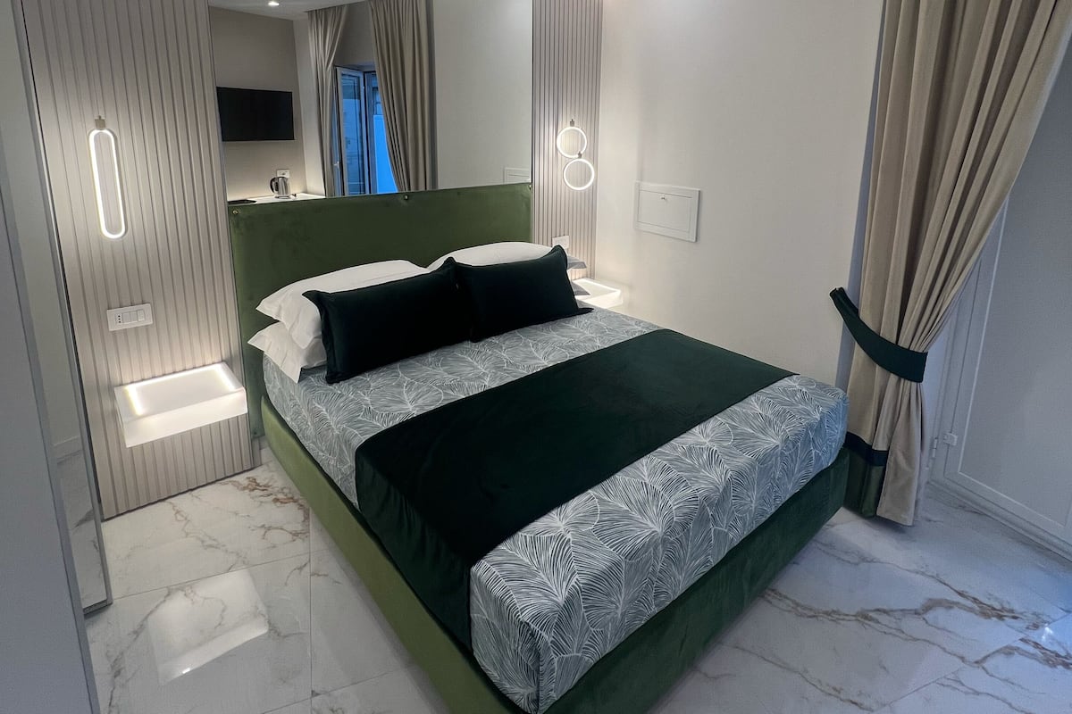 Un dormitorio moderno con una cama grande, una mesita de noche, un espejo y un televisor montado en la pared.