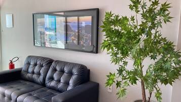 A modern living room with a black leather sofa, a large framed cityscape artwork, and a potted plant.