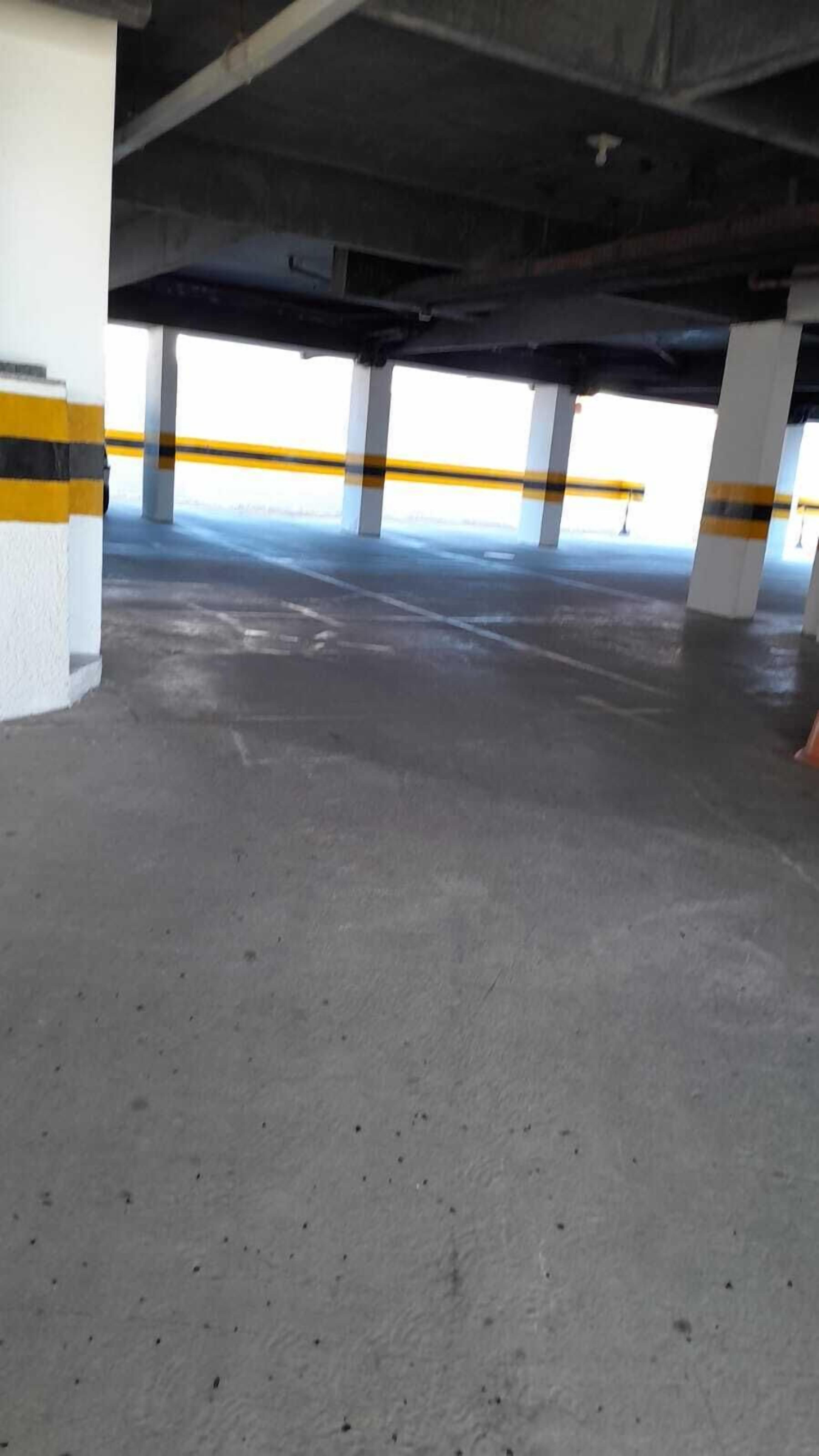 Un estacionamiento vacío con pisos y columnas de concreto, algunas con franjas amarillas.