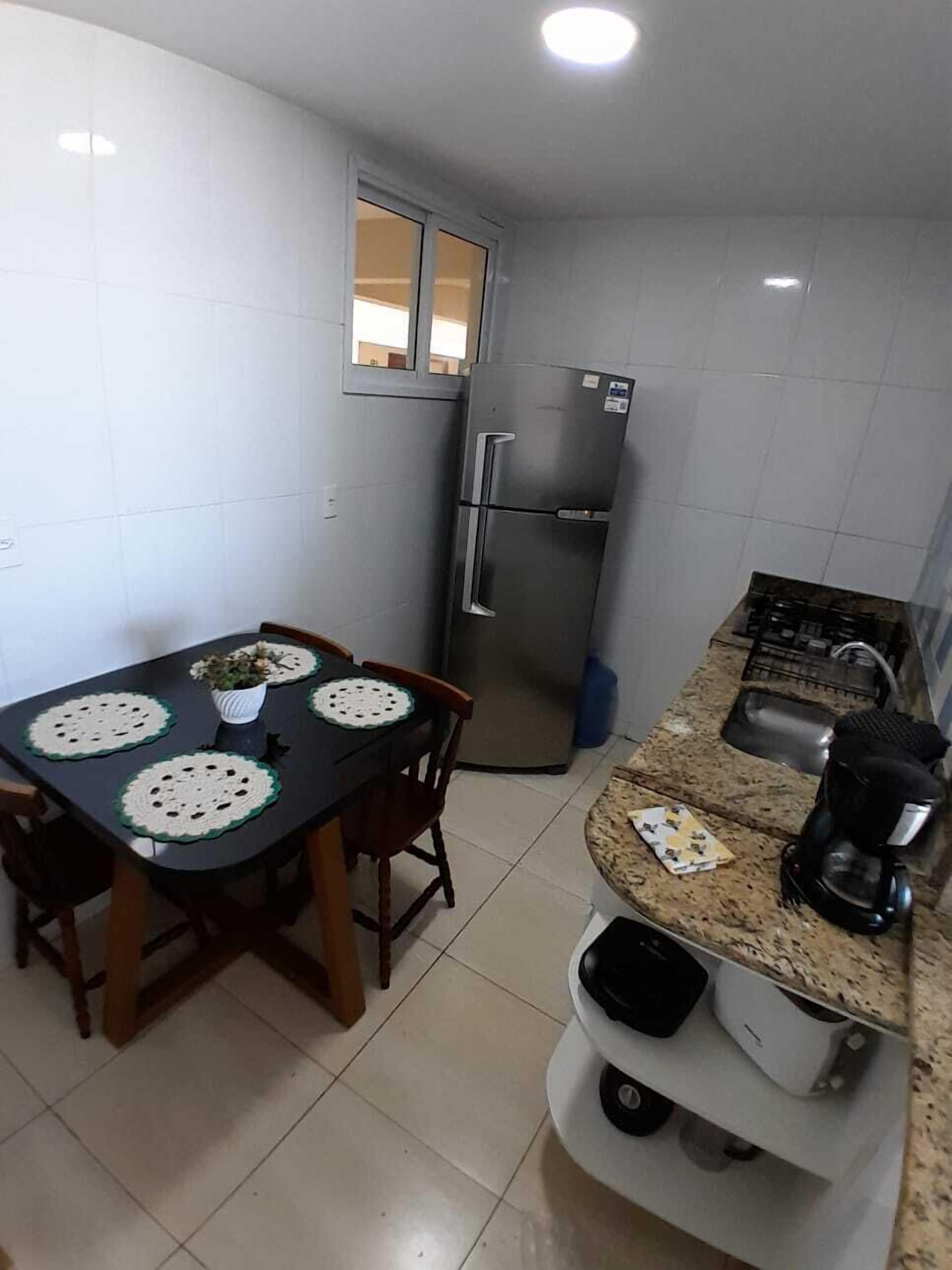 Cocina compacta con refrigerador, una mesa de comedor con sillas y una encimera con cafetera.