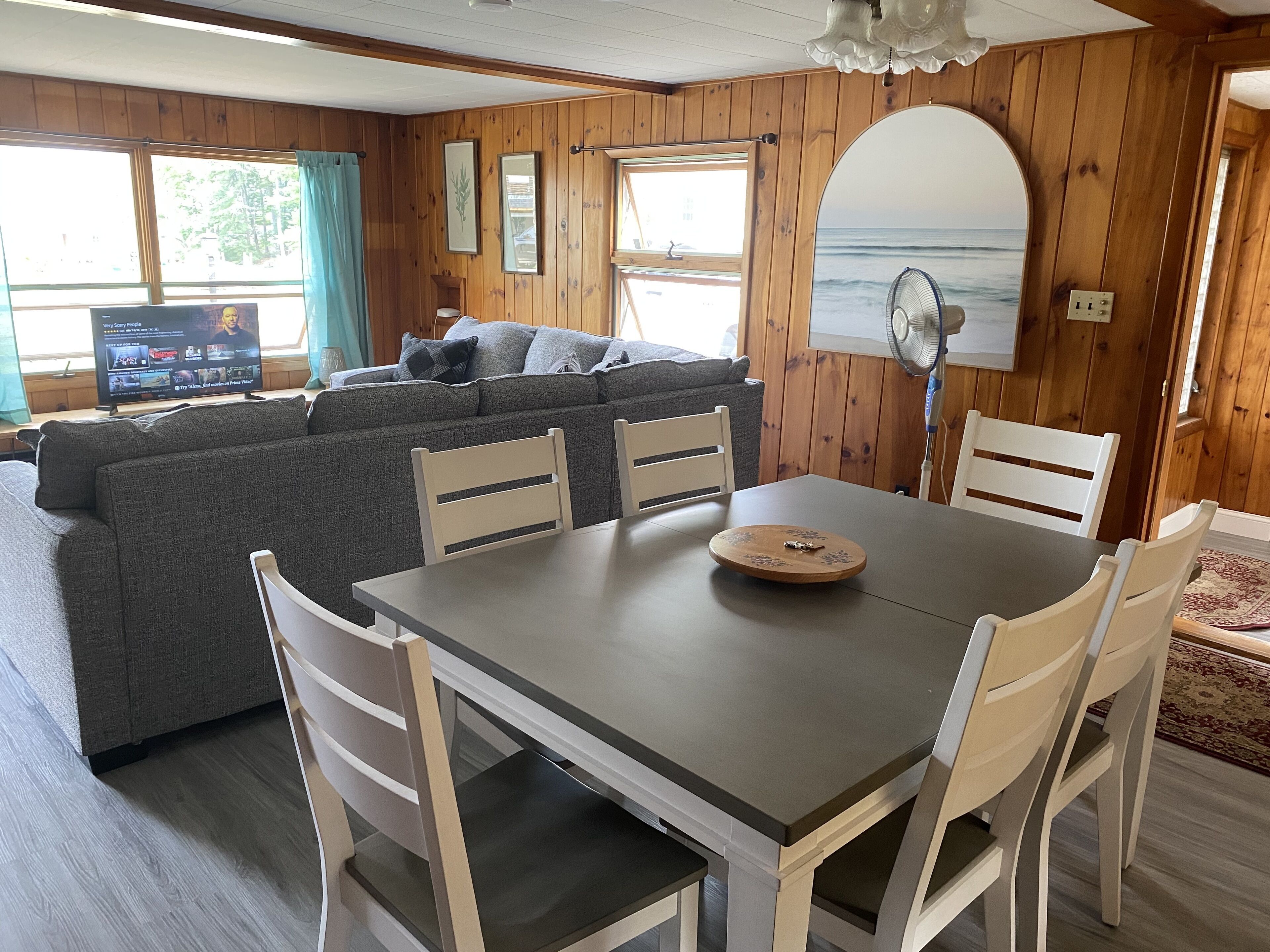 Ein gemütliches Blockhaus-Interieur mit Holzausstattung, einem grauen Sofa, einem Esstisch mit Stühlen und einem großen Fenster mit Meerblick.