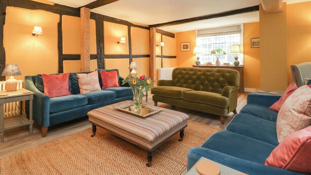 Un salon chaleureux avec un canapé bleu, un fauteuil vert et un pouf à motifs.