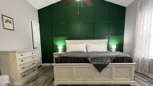 A bedroom with a bed, dresser, and a green accent wall. - Foley Vacation or Monthly Stay Near OWA | Sleeps 12 (Foley)