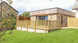 Ein modernes Haus mit einer Natursteinfassade, einer Holzterrasse und einem wolkenlosen Himmel.