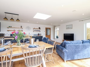 A modern kitchen with a dining area, a living room with a blue sofa, and a TV. - Chi an Mor (Penzance)