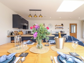 A modern kitchen with dark cabinets, a wooden countertop, and a dining area set for a meal. - Chi an Mor (Penzance)