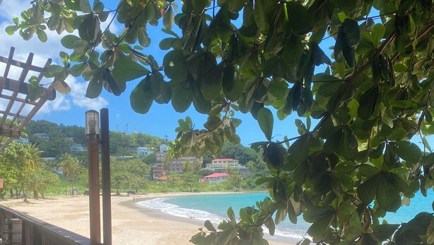 A beach view from a wooden deck with a railing, overlooking a sandy beach and a clear blue sea. - Fabulous poolside apartment Marigot Bay. (Marigot bay)