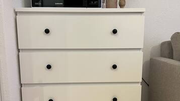 A white chest of drawers with black knobs, a black microwave on top, and a small decorative item beside it.