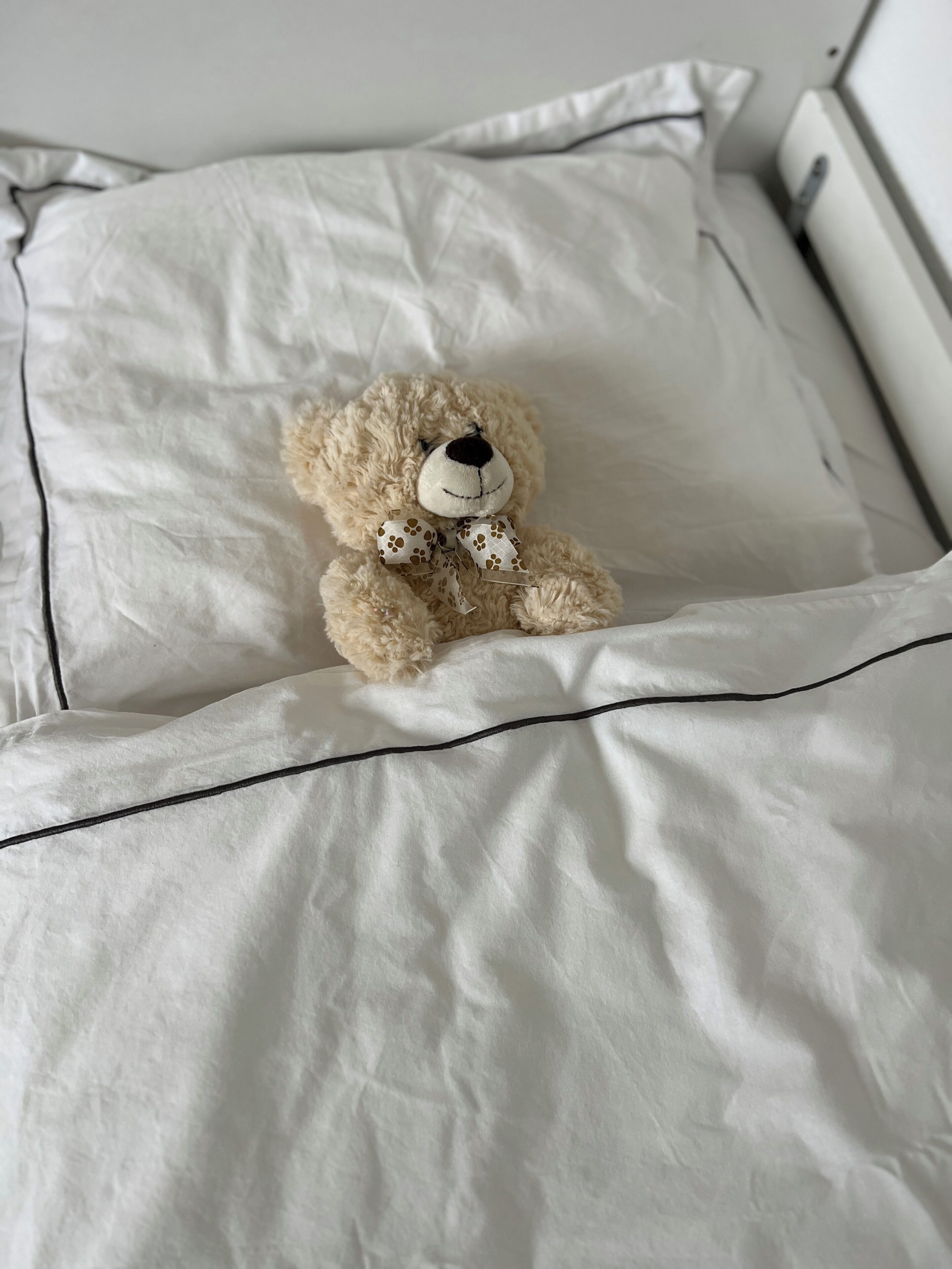 A teddy bear on a bed with white bedding and a black border.