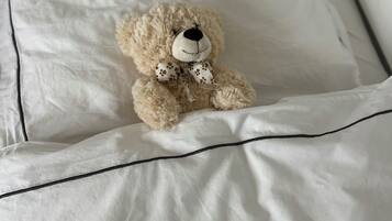A teddy bear on a bed with white bedding and a black border.