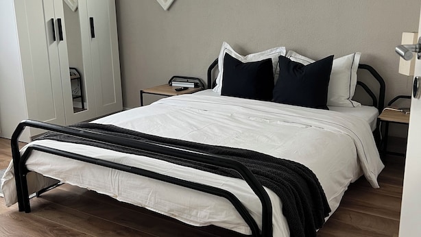 A bedroom with a bed, a wardrobe, a desk, and a hanging light fixture. - Black & White Apartment (Bichwil)