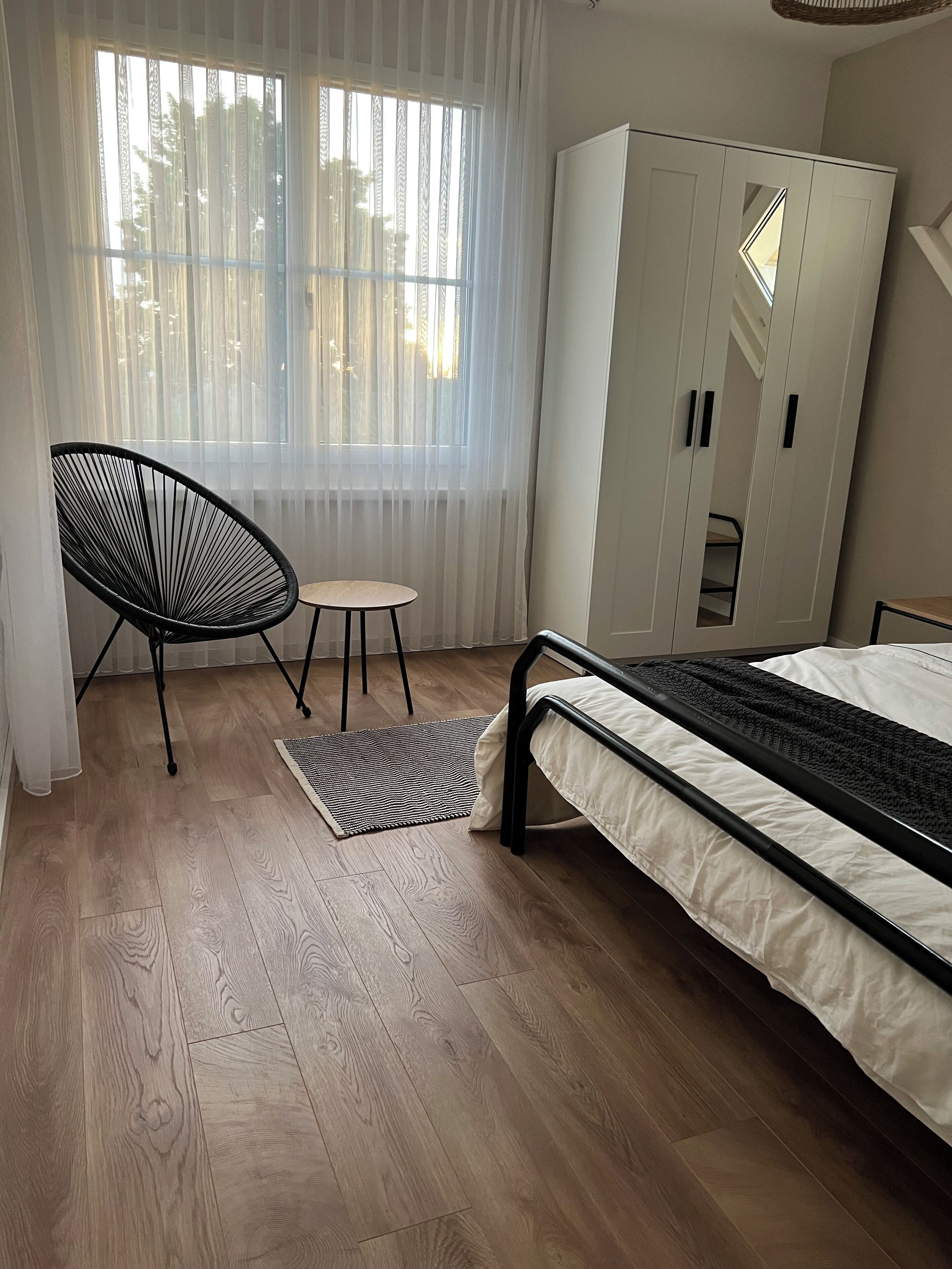 A bedroom with a bed, a chair, a small table, and a wardrobe.