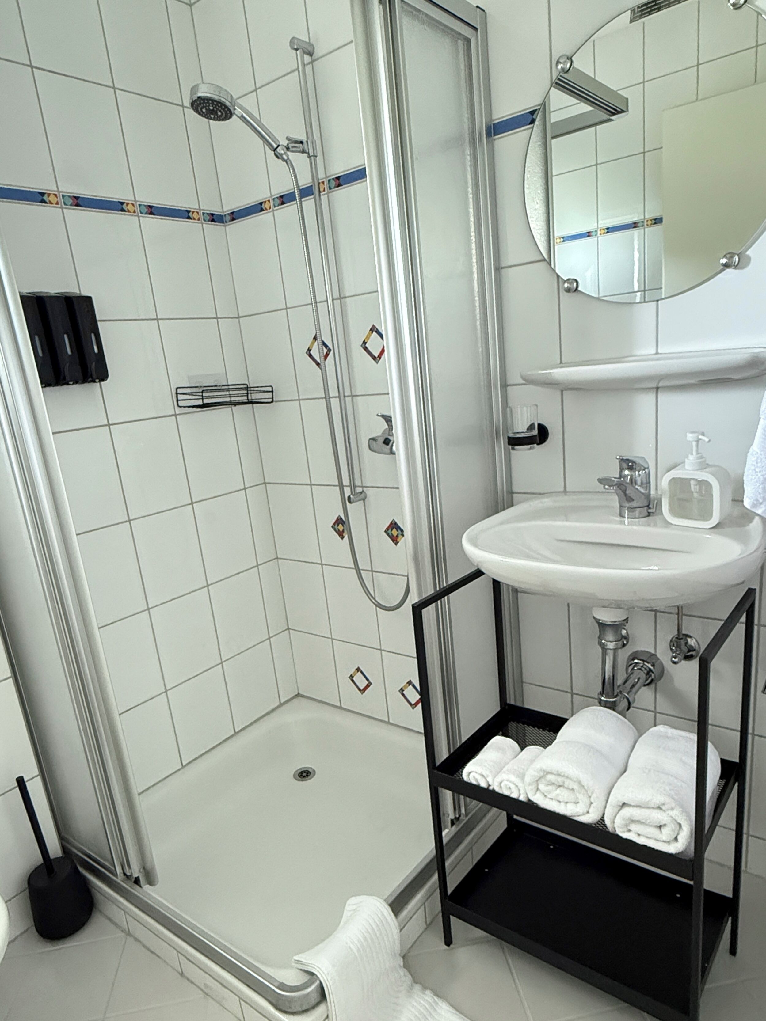 Un bany modern amb dutxa de vidre, un lavabo blanc i una barra de tovalloles negra.