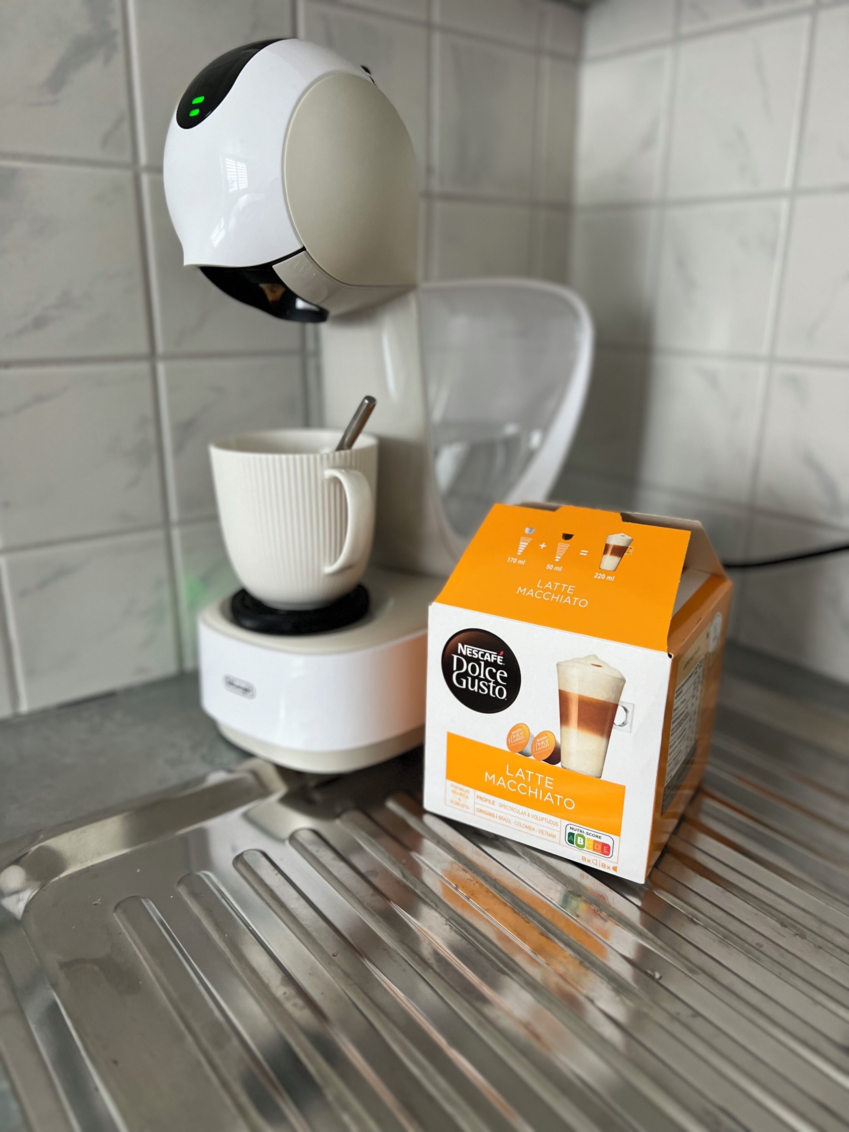A Nescafe Dolce Gusto coffee machine with a cup and saucer, and a box of Latte Macchiato coffee.