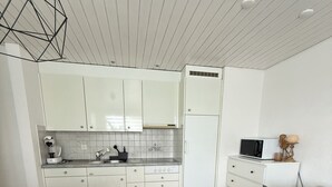 A modern kitchen with white cabinets, a microwave, and a coffee maker. There is a dining table with chairs and a sofa with a cushion. - Black & White Apartment (Bichwil)