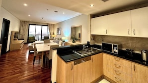 A modern kitchen with wooden cabinets and a black countertop, a dining area with a table and chairs, and a balcony with a view. - Lux BnB I Palm Jumeirah Resort I Palm Views (Dubai)