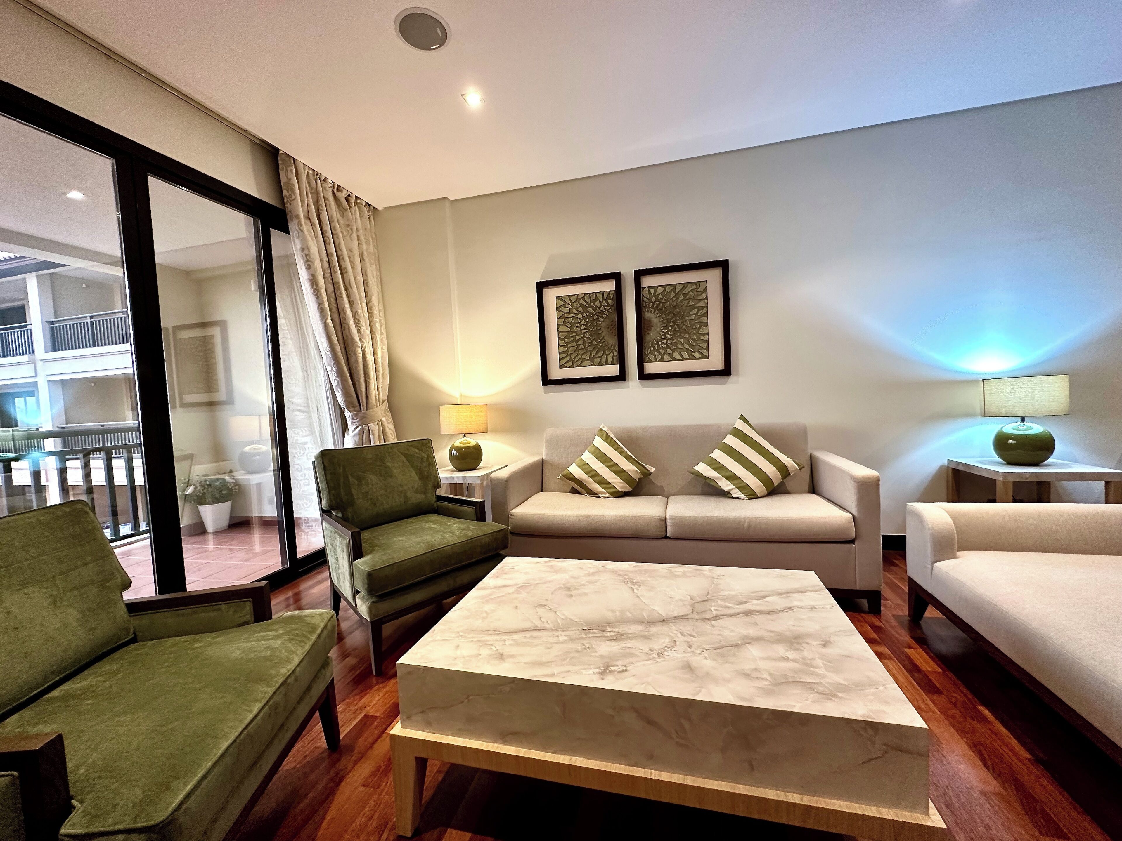 A modern living room with a sofa, armchairs, a marble coffee table, and a glass door leading to a balcony.