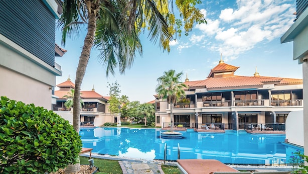 A swimming pool with lounge chairs, a palm tree, and a building with a tiled roof. - Lux BnB I Palm Jumeirah Resort I Palm Views (Dubai)
