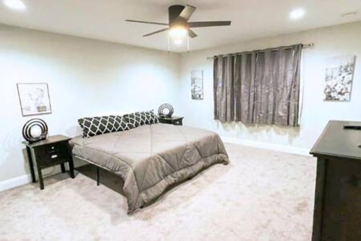 A bedroom with a bed, a nightstand, a ceiling fan, and a window with curtains.