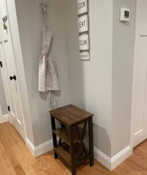 A small wooden stool in a hallway with a wall-mounted sign listing kitchen-related tasks.