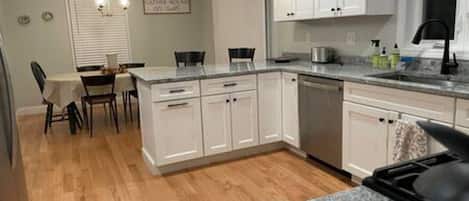 A kitchen with white cabinets, a granite countertop, and a dining area with a table and chairs.