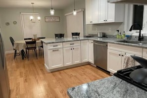 Une cuisine avec des meubles blancs, un plan de travail en granit et un coin repas comprenant une table et des chaises.