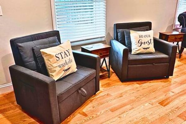 Two leather armchairs with pillows, one with 'STAY' and the other with 'BE OUR Guest,' in a room with wooden flooring.