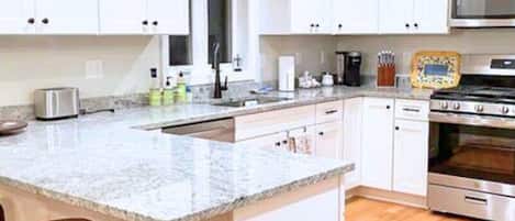 Una cocina con armarios blancos, encimera de granito, horno de acero inoxidable y microondas.