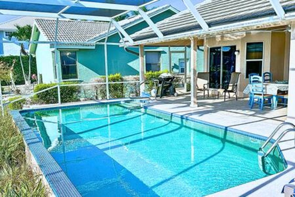 A swimming pool with a covered patio area, a table, and chairs.