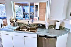 A kitchen with a double sink, a dishwasher, and a window with a view of the outside.