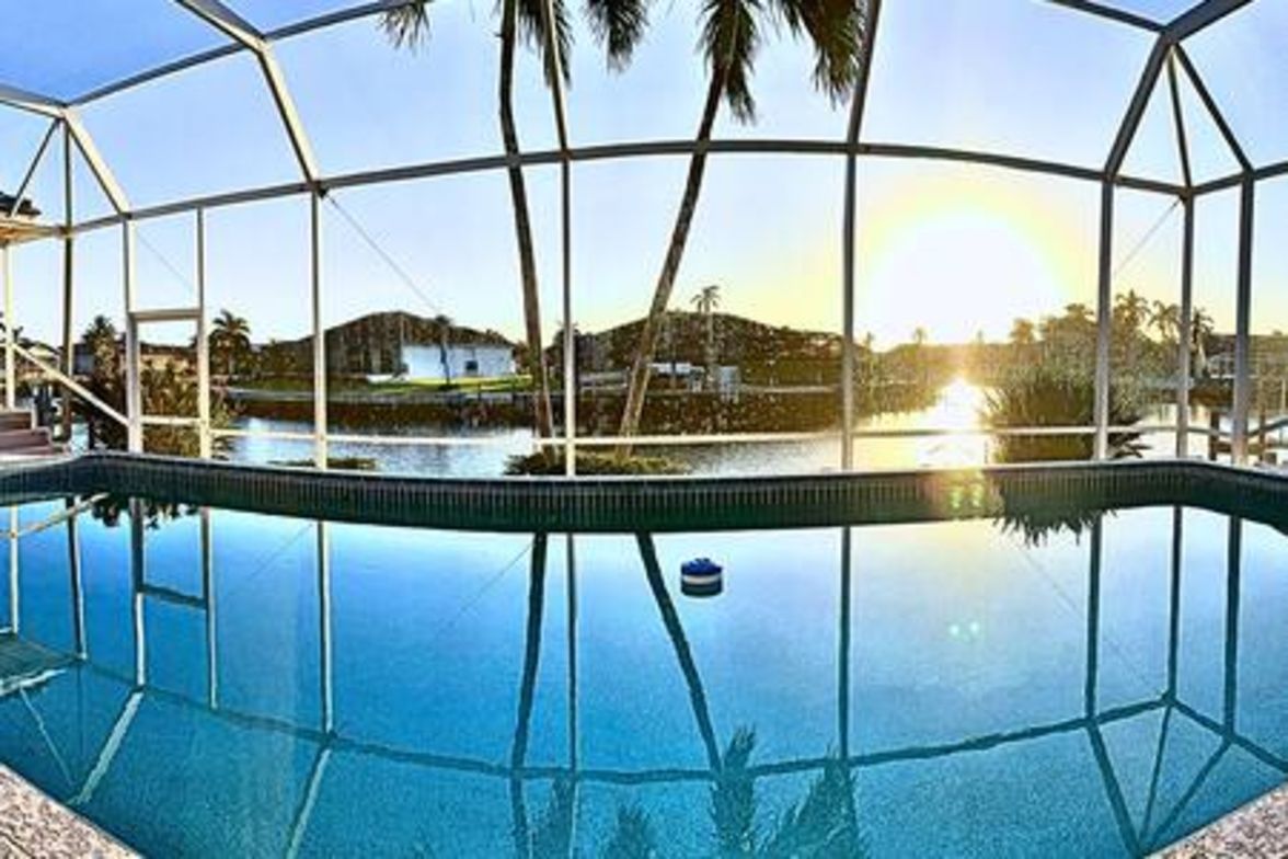 A clear pool with a metal frame structure, surrounded by palm trees and a view of distant hills.