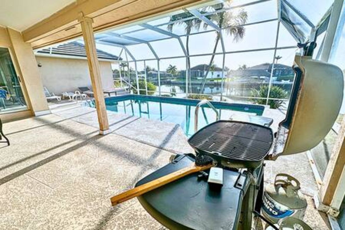 A covered outdoor area with a grill, a pool, and lounge chairs.