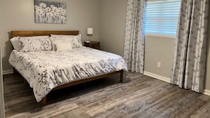 Quarto com cama de madeira, ventoinha no teto, mesa de cabeceira, luminária na parede e janela com cortinas.
