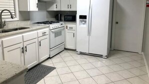 Uma cozinha com armários brancos, fogão, geladeira e micro-ondas.
