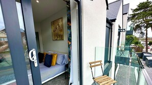 A modern apartment with a glass balcony, a sofa with cushions, and a painting on the wall.
