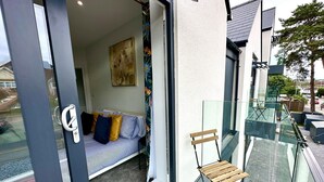 A modern apartment with a glass balcony, a sofa with cushions, and a painting on the wall. - Stunning Brand New House - Sleeps 6 - Free Parking (Poole)
