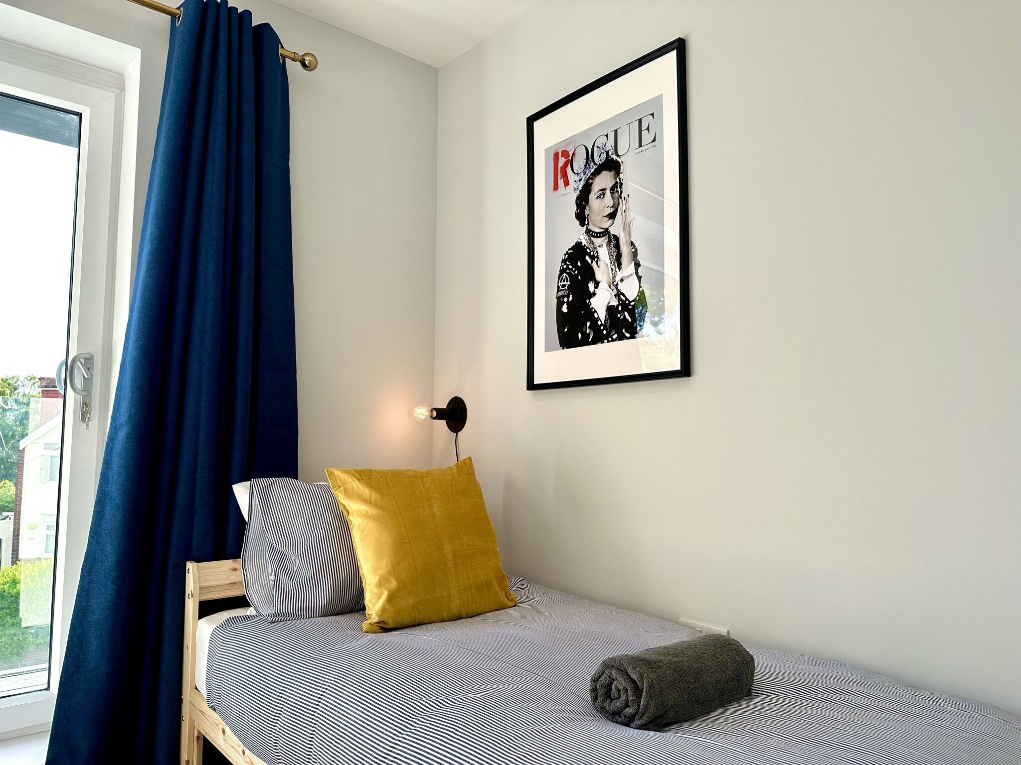 A bedroom with a bed, a framed magazine on the wall, and a window with curtains.