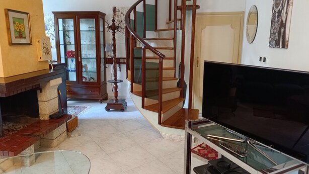 Una sala de estar con una escalera de madera, una chimenea, una mesa de centro de vidrio y un televisor de pantalla plana.