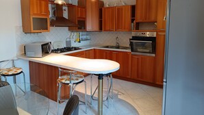 Una cocina con gabinetes de madera, una estufa a gas, un microondas, un lavaplatos y un refrigerador. Hay dos taburetes de bar con cojines estampados.