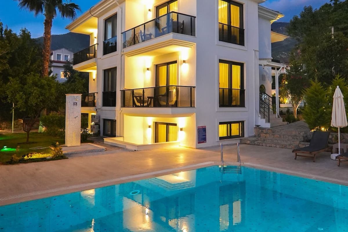 A multi-story building with balconies, a swimming pool, and a well-lit exterior.