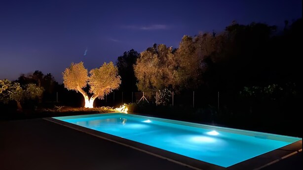 Piscina retangular à noite, com árvores iluminadas e céu limpo.