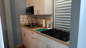 Pieni, käytännöllinen keittiö, jossa on valkoiset kaapit, musta mikroaaltouuni, kahvinkeitin ja liesi.