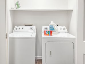 A laundry area with two white washing machines and a bottle of detergent.