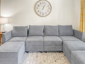 Un canapé d’angle gris, avec une horloge accrochée au mur derrière.