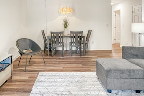 Un salon moderne avec un canapé gris, un coin repas comprenant une table et des chaises, et un tapis à motifs.