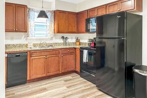 Une cuisine avec des meubles de rangement en bois, un réfrigérateur noir, un four à micro-ondes et un lave-vaisselle.