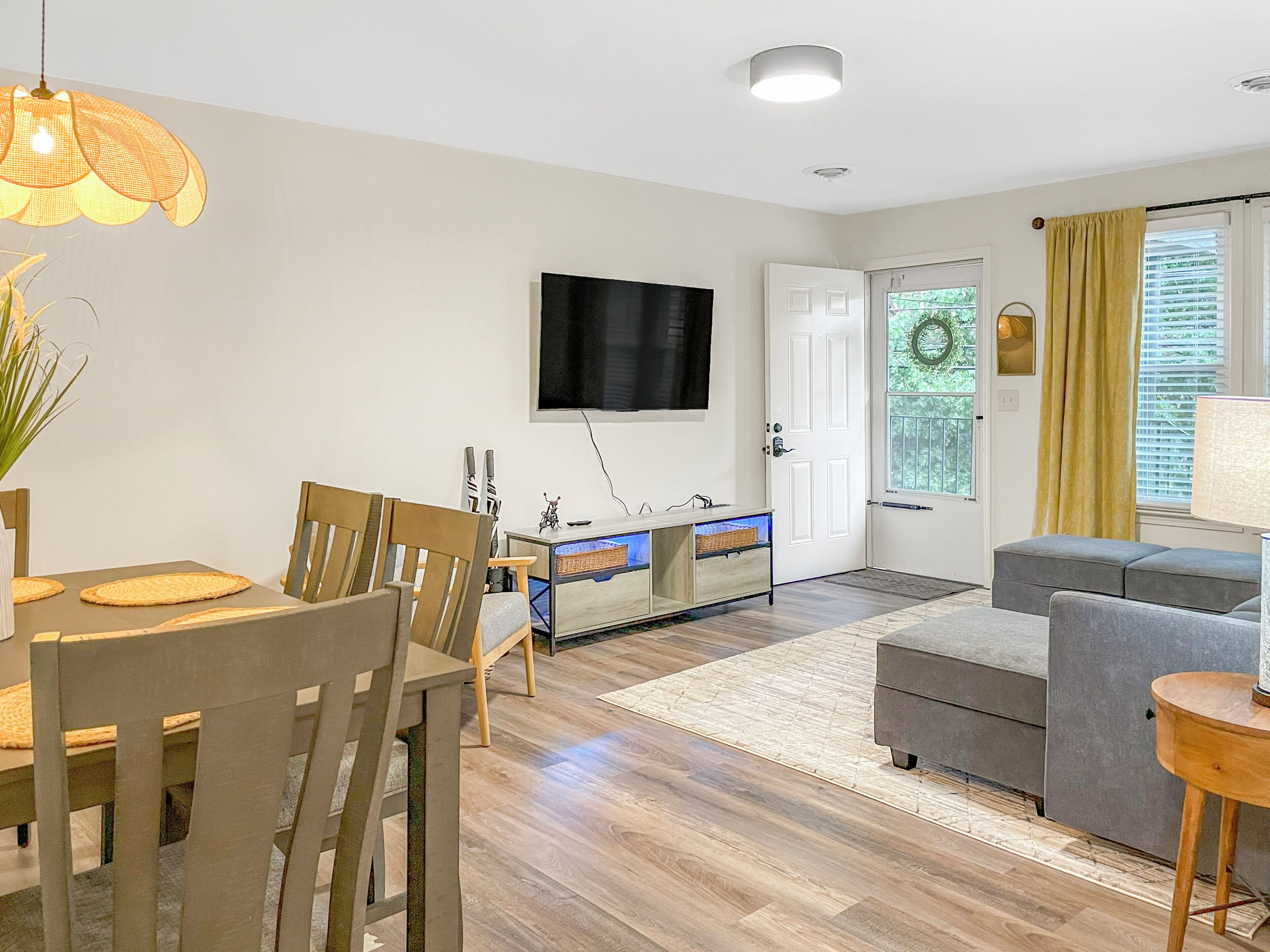Een moderne woonkamer met een eethoek, een flatscreen televisie aan de muur en een deur naar een buitenruimte.