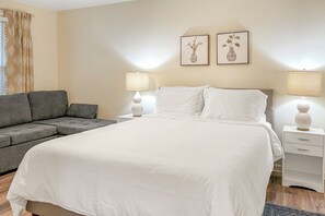 A hotel room with a bed, a grey sofa, two bedside lamps, and two framed pictures on the wall.