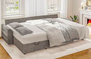 A bed with a grey headboard, white bedding, and a patterned throw.
