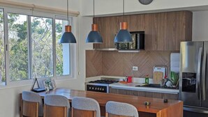 Cocina moderna con una isla central, taburetes de bar, refrigerador de acero inoxidable y un revestimiento de madera en patrón de espiga.